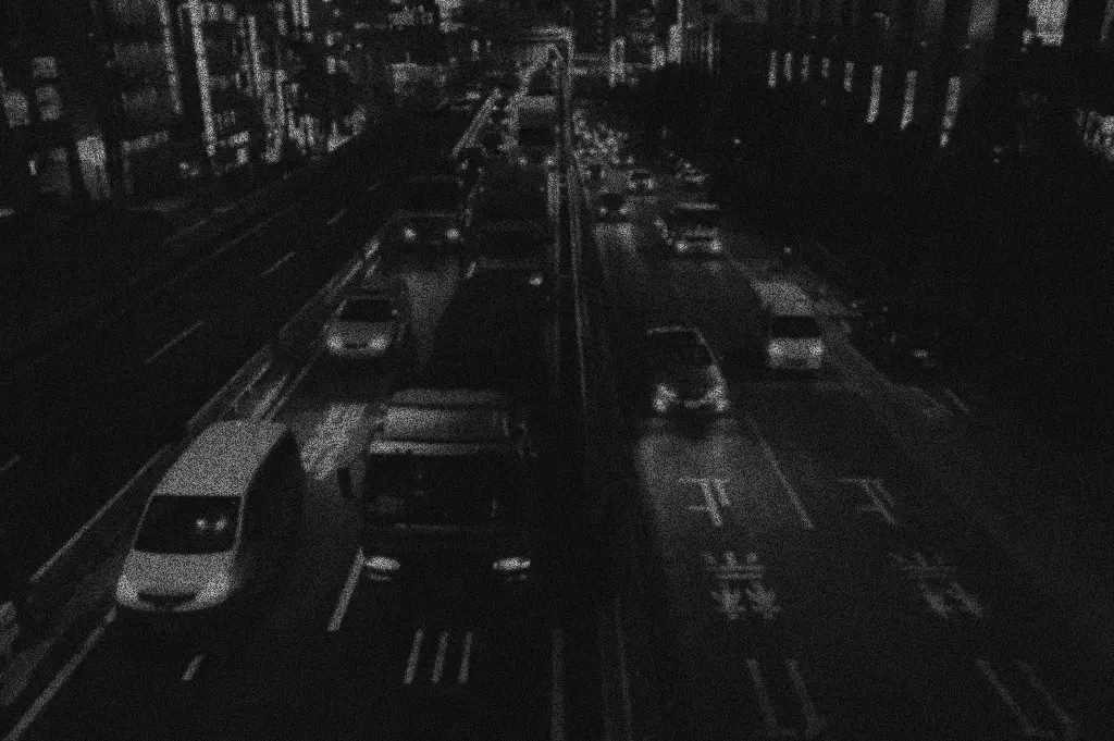 The same street at night through a conventional camera: grainy black and white, the taxis hard to tell apart