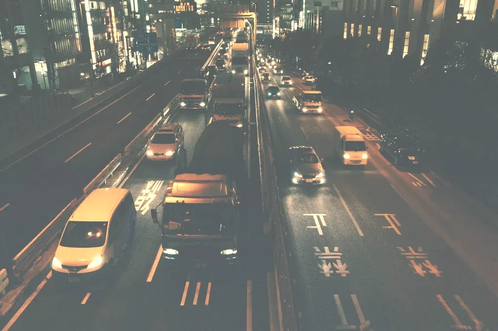 A city street at dusk: taxis and cars heading in under the first streetlights